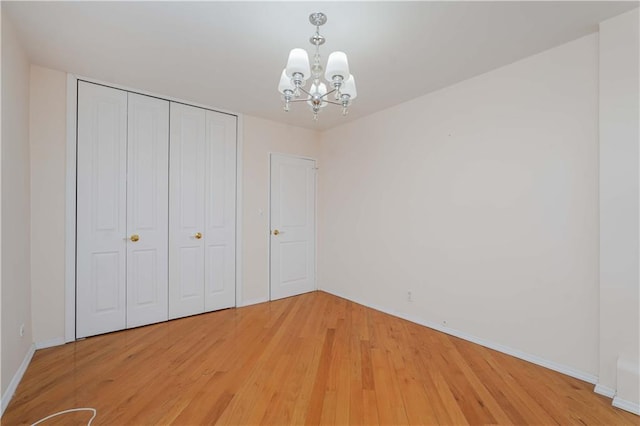 unfurnished bedroom featuring a chandelier, baseboards, light wood-type flooring, and a closet