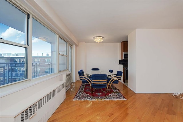 dining room with a wall mounted air conditioner, radiator heating unit, and light wood finished floors