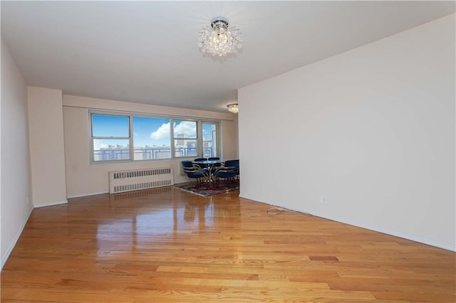 unfurnished room featuring a notable chandelier, radiator, and wood finished floors