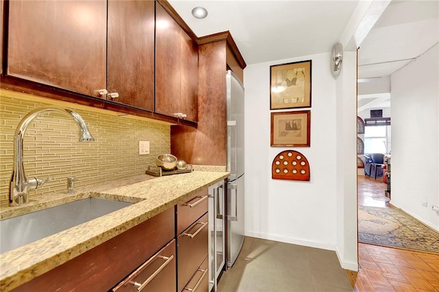 kitchen with backsplash, light stone counters, stainless steel refrigerator, and sink