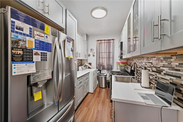 kitchen featuring decorative backsplash, stainless steel refrigerator with ice dispenser, sink, light hardwood / wood-style flooring, and washer / clothes dryer