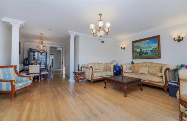 living room with ornate columns, ornamental molding, a notable chandelier, and light hardwood / wood-style floors