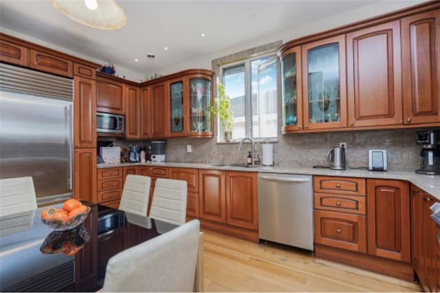 kitchen featuring decorative backsplash, built in appliances, sink, and light hardwood / wood-style flooring