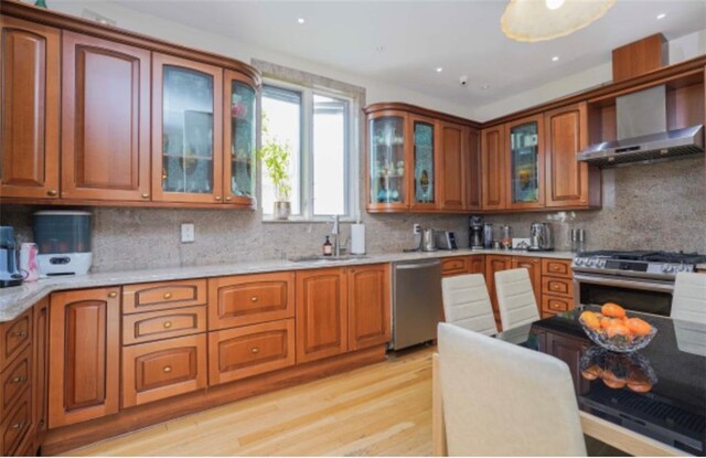 kitchen with appliances with stainless steel finishes, sink, decorative backsplash, light hardwood / wood-style floors, and wall chimney range hood