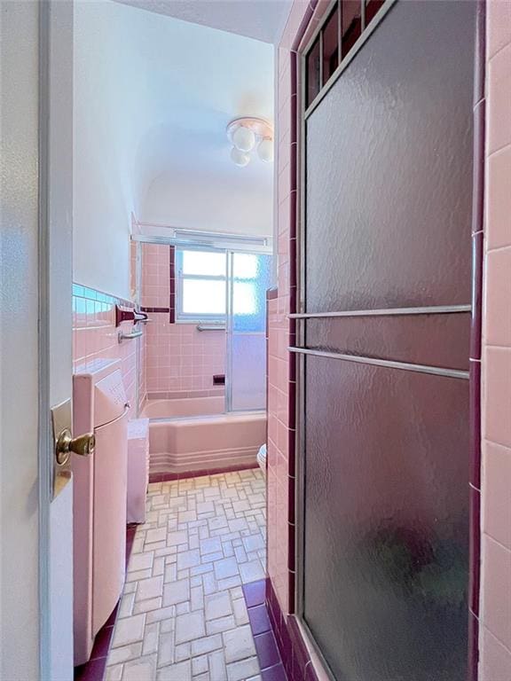 bathroom featuring combined bath / shower with glass door, toilet, and tile walls