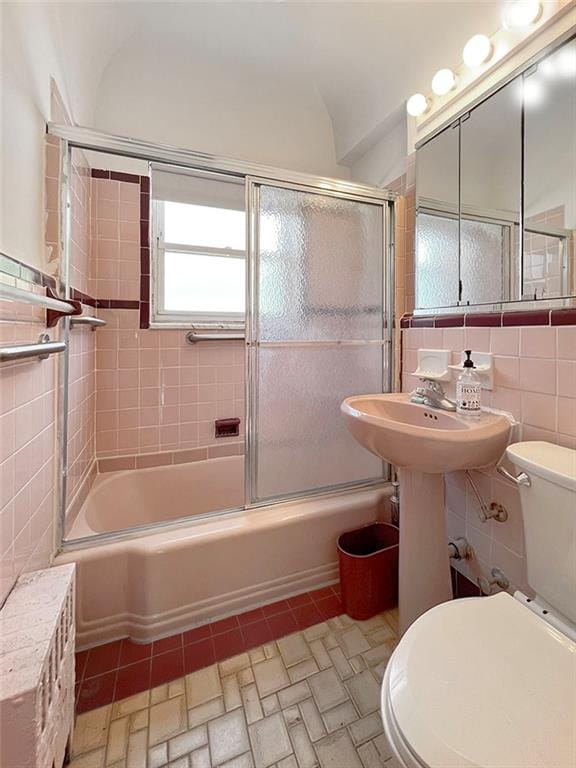 bathroom featuring toilet, combined bath / shower with glass door, and tile walls