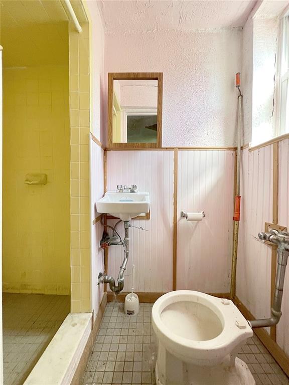 bathroom with tiled shower, tile patterned flooring, toilet, and sink