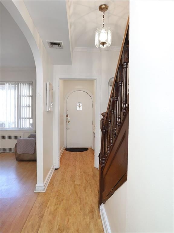 entrance foyer with light hardwood / wood-style floors, radiator heating unit, crown molding, and a chandelier