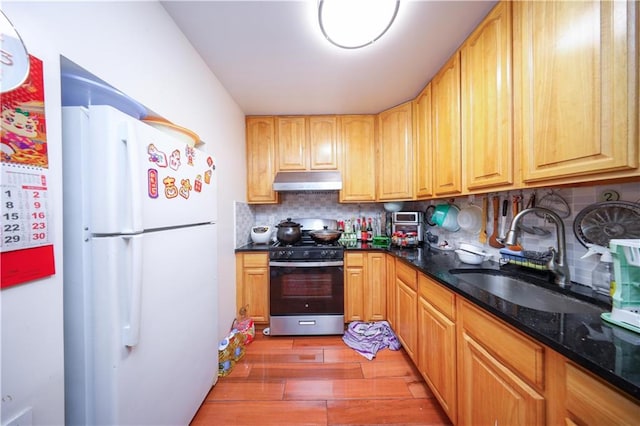 kitchen with backsplash, white refrigerator, stainless steel range with gas cooktop, sink, and dark hardwood / wood-style floors