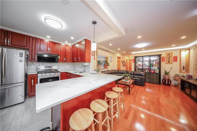 kitchen featuring a kitchen bar, appliances with stainless steel finishes, ventilation hood, and hanging light fixtures