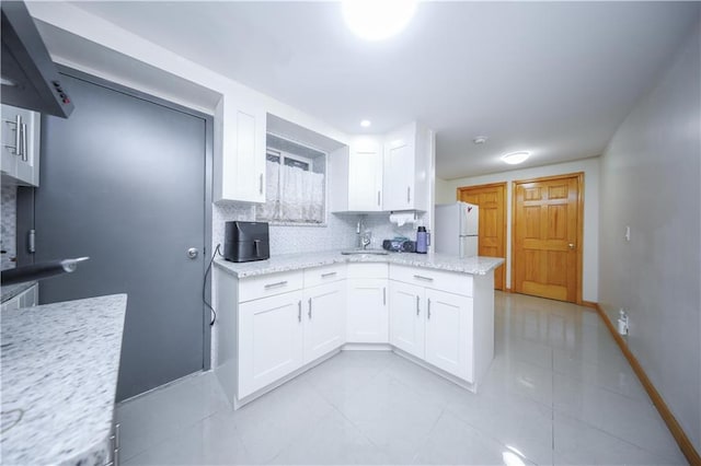 kitchen featuring sink, decorative backsplash, light stone countertops, white fridge, and white cabinetry