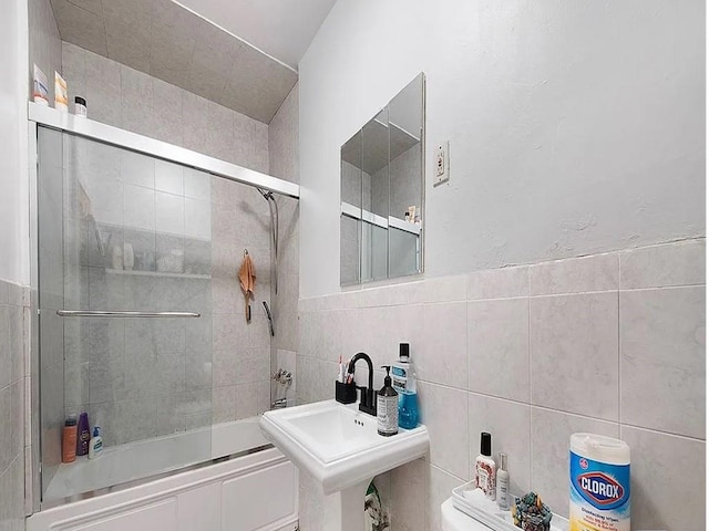 full bathroom featuring toilet, shower / bath combination with glass door, sink, and tile walls