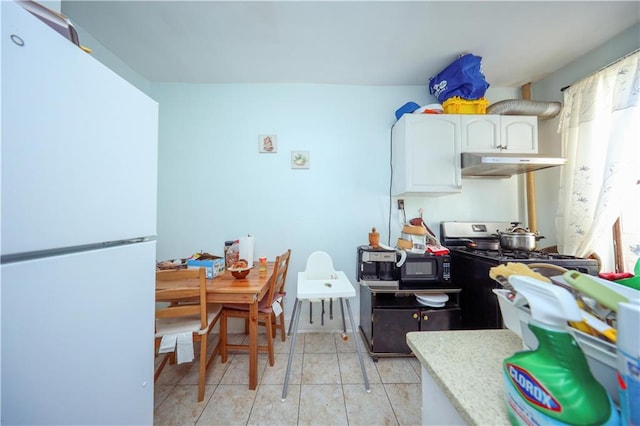 kitchen with black microwave, stainless steel range with gas stovetop, freestanding refrigerator, under cabinet range hood, and white cabinetry