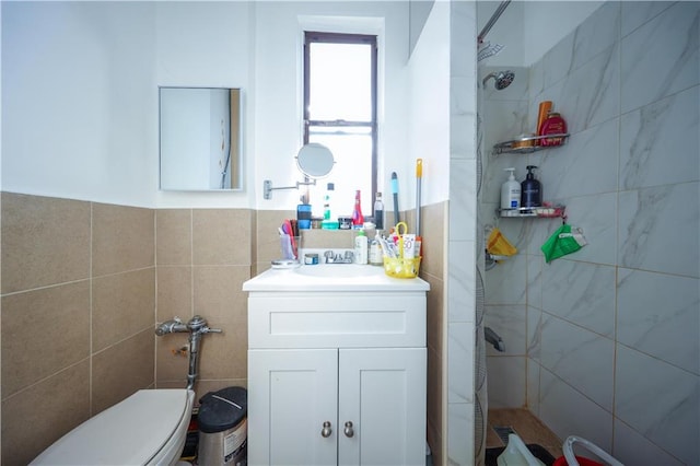 bathroom with toilet, a tile shower, tile walls, and vanity