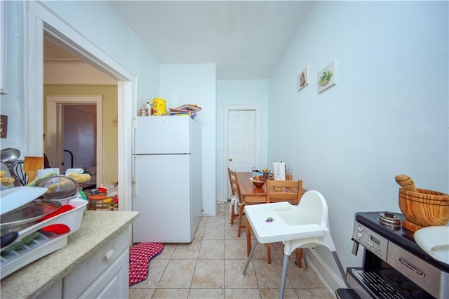 kitchen with freestanding refrigerator, white cabinets, light countertops, and light tile patterned floors