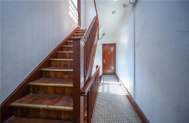staircase with baseboards, a textured wall, and carpet