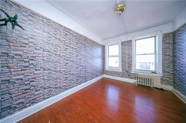 spare room with dark wood-type flooring, a textured ceiling, radiator, and baseboards