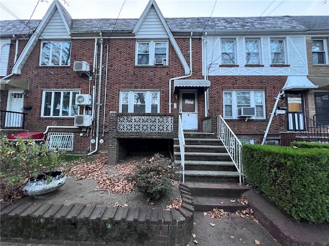 view of property featuring brick siding, a wall mounted air conditioner, and cooling unit