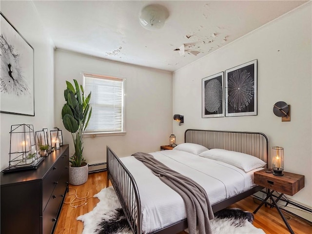 bedroom with a baseboard heating unit and light hardwood / wood-style floors