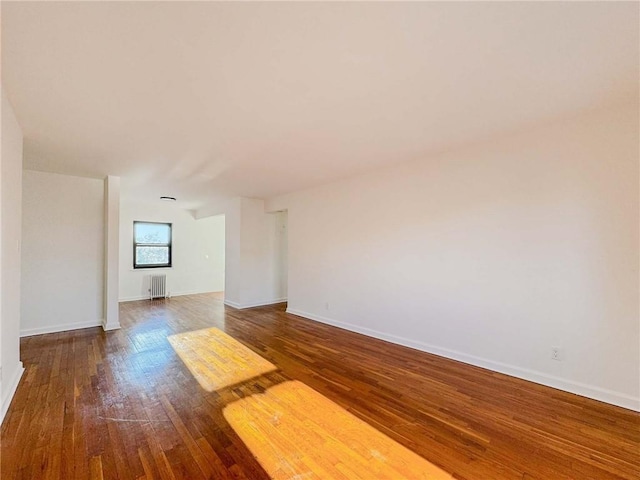 spare room featuring baseboards, wood-type flooring, and radiator heating unit