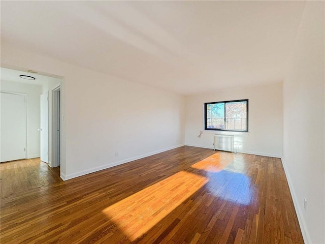 spare room with radiator, baseboards, and wood-type flooring