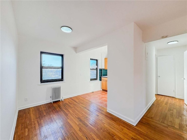 empty room with radiator, light wood-type flooring, and baseboards