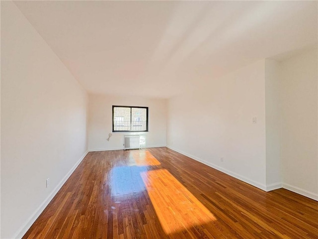 empty room featuring baseboards, radiator, and wood finished floors