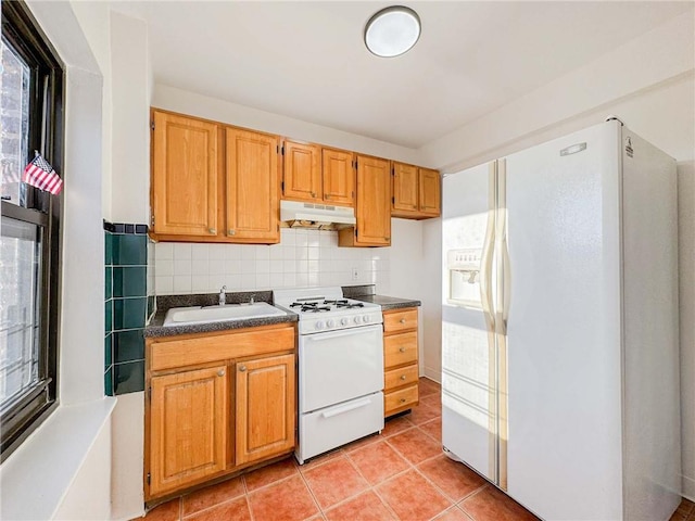 kitchen featuring under cabinet range hood, a sink, dark countertops, white appliances, and light tile patterned floors