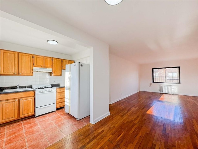 kitchen with white appliances, under cabinet range hood, radiator, a sink, and light wood finished floors