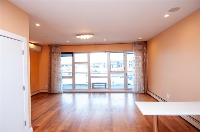 spare room featuring baseboard heating, an AC wall unit, and light hardwood / wood-style floors