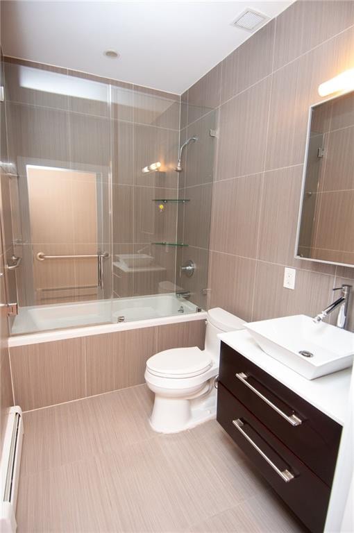 full bathroom with toilet, tiled shower / bath, baseboard heating, tile walls, and vanity