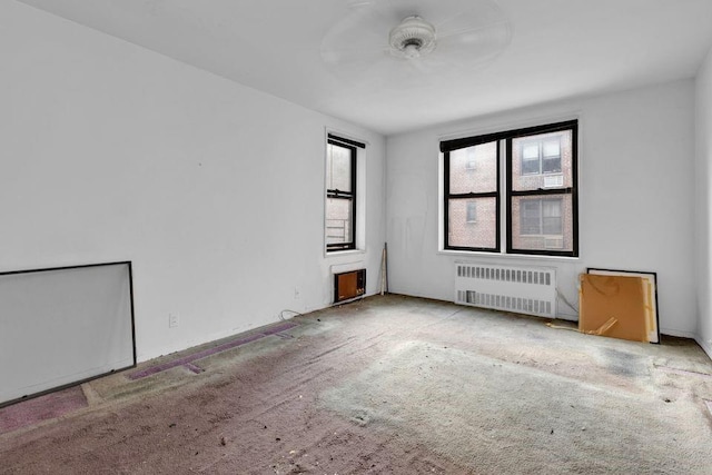 spare room featuring ceiling fan, radiator heating unit, and light carpet