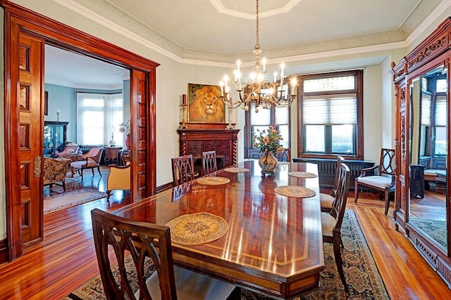 dining area featuring a brick fireplace, crown molding, hardwood / wood-style floors, and a notable chandelier