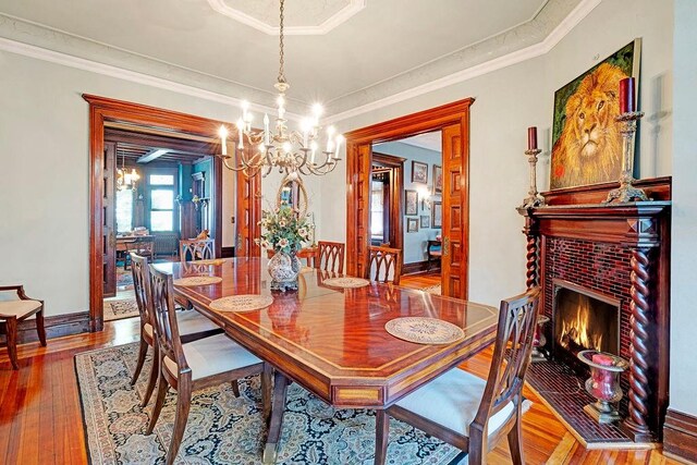 dining space featuring an inviting chandelier, hardwood / wood-style flooring, a brick fireplace, and crown molding