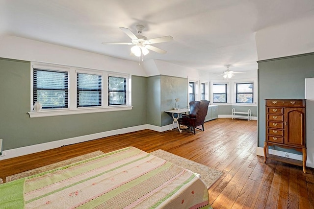 unfurnished bedroom featuring hardwood / wood-style floors, ceiling fan, multiple windows, and radiator