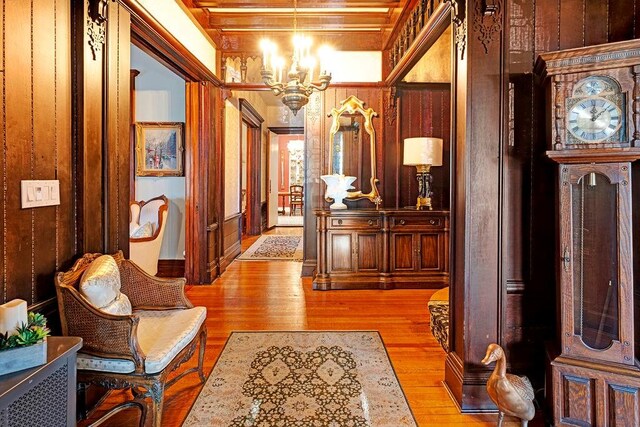 hall featuring wooden walls, light hardwood / wood-style flooring, and a chandelier