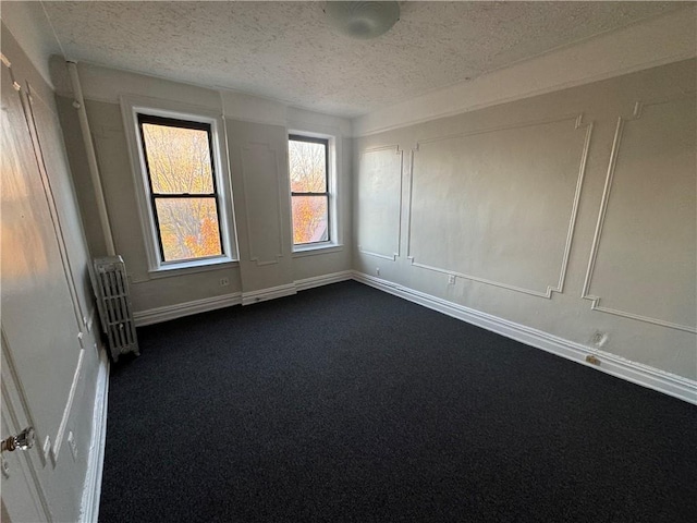 empty room with radiator, dark carpet, and a textured ceiling