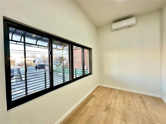 empty room with a wall mounted AC, vaulted ceiling, and light wood-type flooring