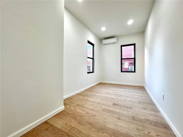 empty room featuring an AC wall unit, light wood finished floors, baseboards, and recessed lighting