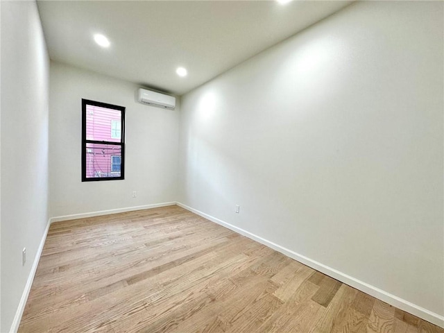 empty room featuring a wall mounted AC, light wood-type flooring, baseboards, and recessed lighting