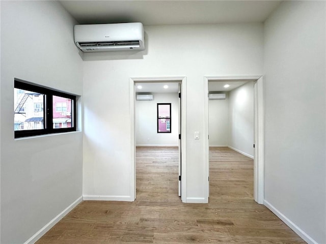 hall featuring a towering ceiling, baseboards, wood finished floors, and a wall mounted air conditioner