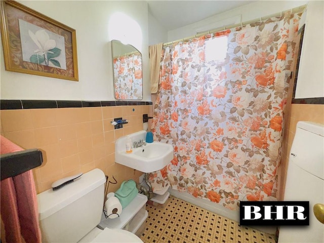 full bathroom featuring tile walls, toilet, tile patterned floors, a sink, and a wainscoted wall