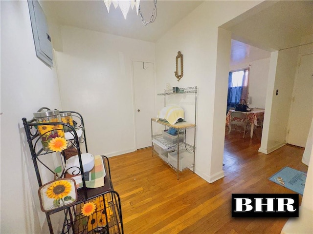 corridor with light wood-type flooring, a chandelier, electric panel, and baseboards