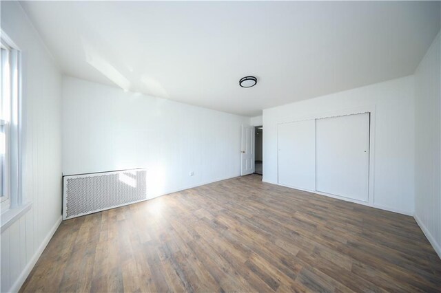 unfurnished bedroom with a closet, dark hardwood / wood-style floors, and radiator heating unit