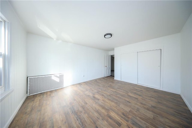 unfurnished bedroom with a closet, radiator heating unit, and wood finished floors