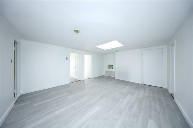 additional living space with light wood-type flooring, a skylight, and baseboards