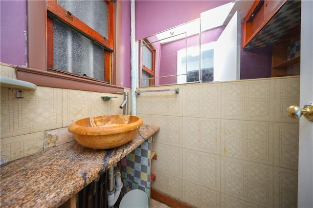 half bathroom with tasteful backsplash, a sink, and tile walls