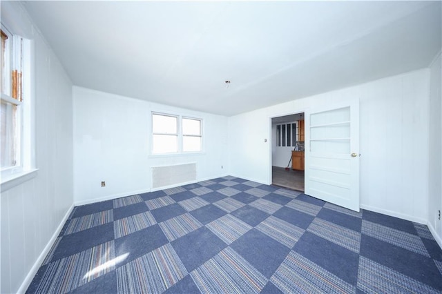 spare room featuring built in shelves, baseboards, and dark colored carpet