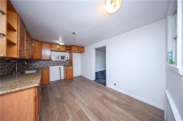 kitchen with decorative backsplash, white microwave, wood finished floors, open shelves, and a sink