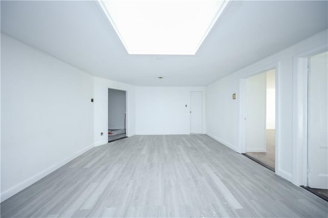 spare room with light wood-type flooring, a skylight, and baseboards